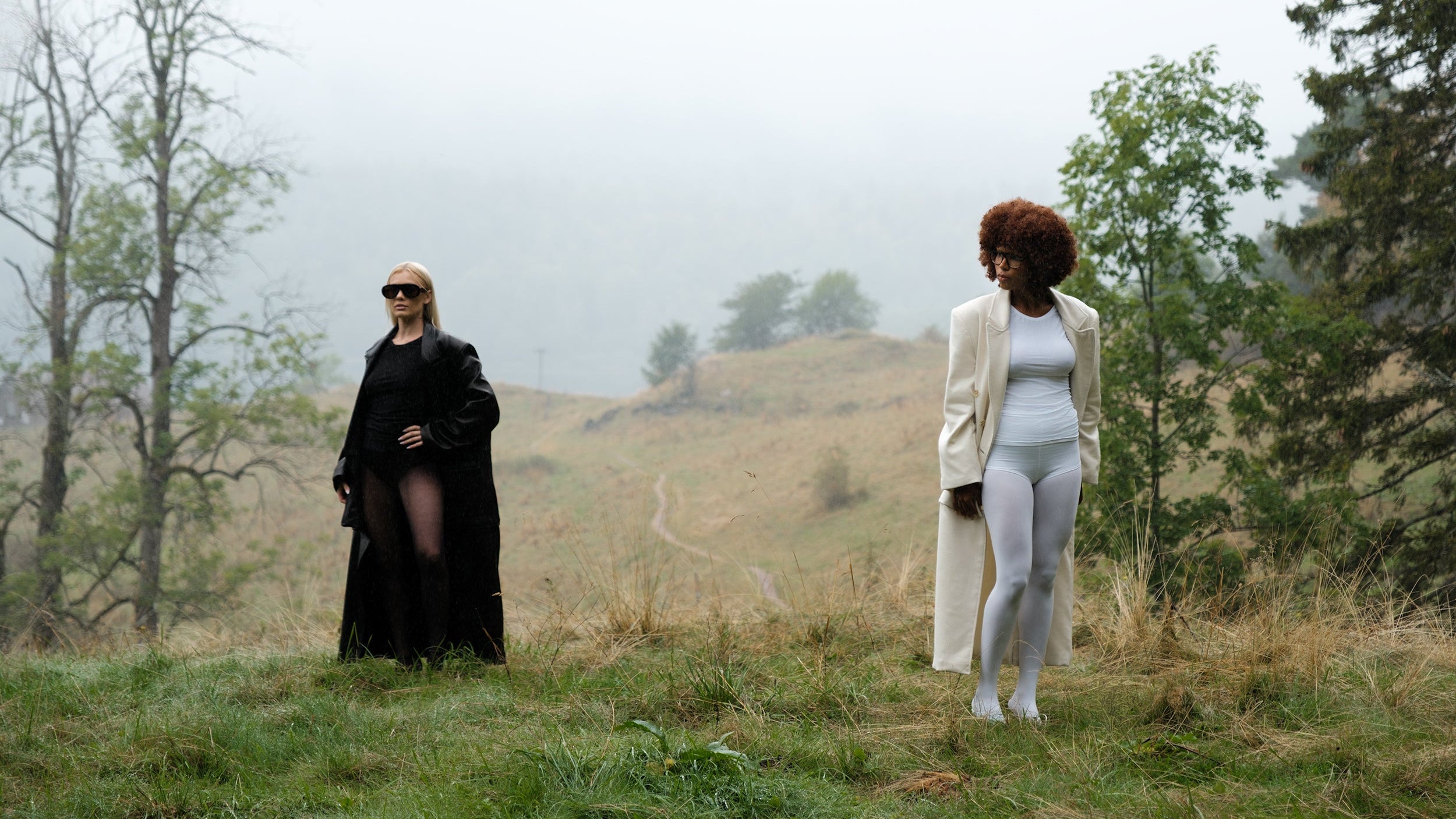 Two women standing in a misty field with trees in the background